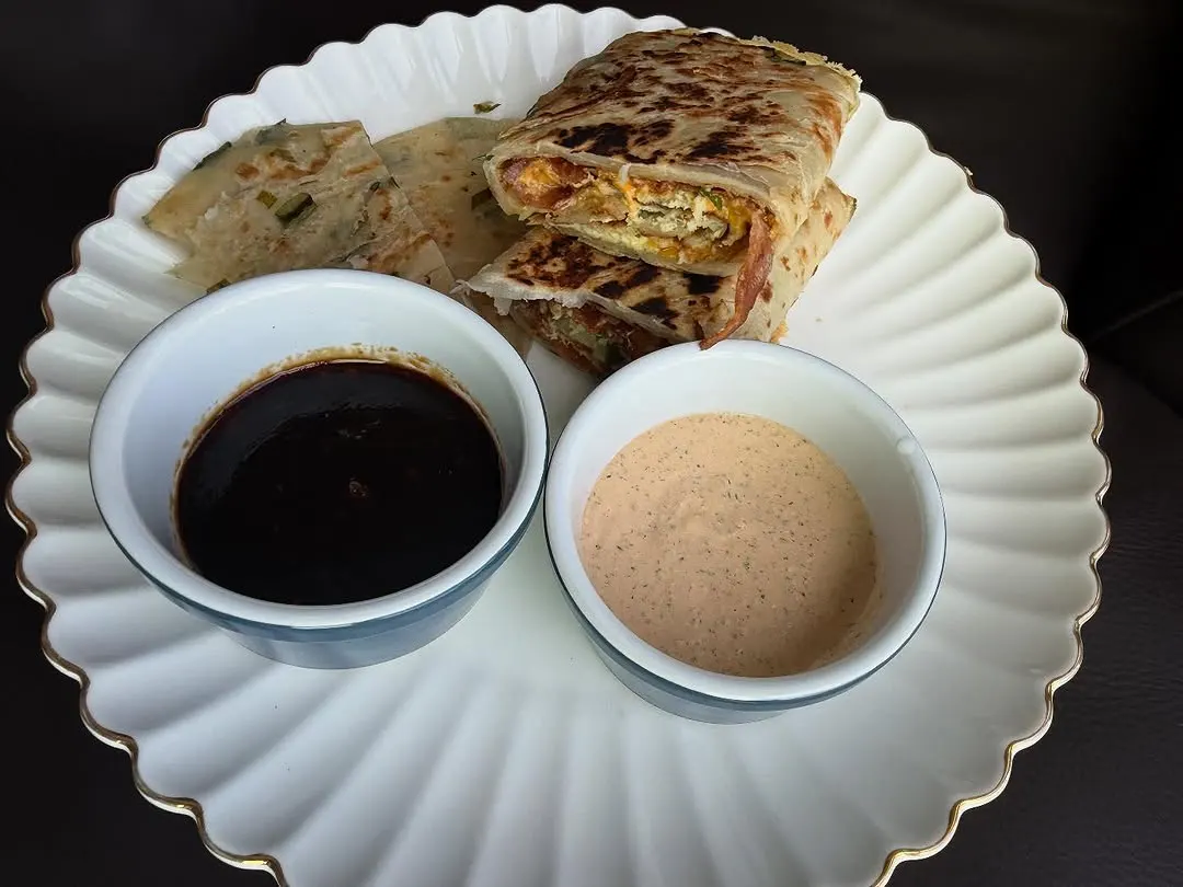 A scallion pancake wrap plated with two dipping sauces.